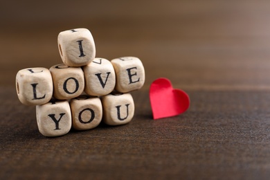 Cubes with words I Love You and paper heart on wooden table