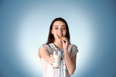 Beautiful young woman drinking milk with cookie on color background