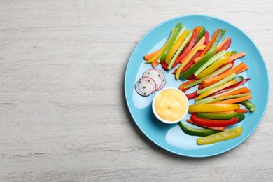 Photo of Different vegetables cut in sticks and dip sauce on light wooden table, top view. Space for text