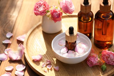 Photo of Bottles of rose essential oil and flowers on wooden table