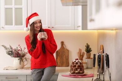 Beautiful young woman in Santa hat with cup of tea in kitchen. Celebrating Christmas