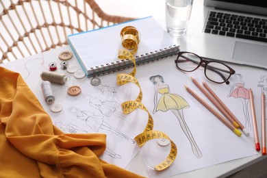 Sketches of clothes and different stuff on white table. Fashion designer's workplace