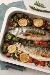 Photo of Delicious fish with vegetables and lemon in baking dish on light marble table, top view