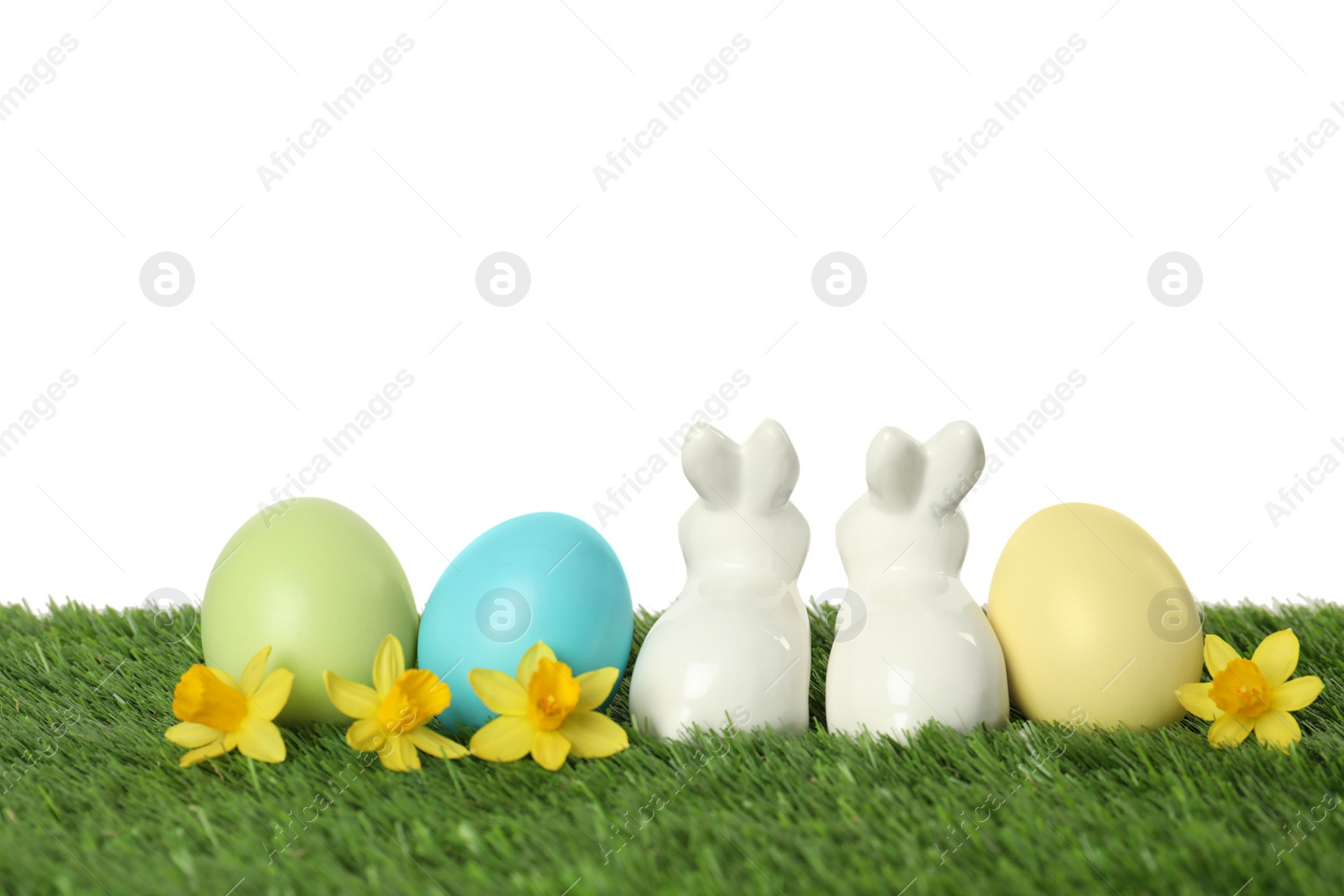 Photo of Ceramic Easter bunny and dyed eggs on green grass against white background