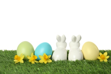 Photo of Ceramic Easter bunny and dyed eggs on green grass against white background