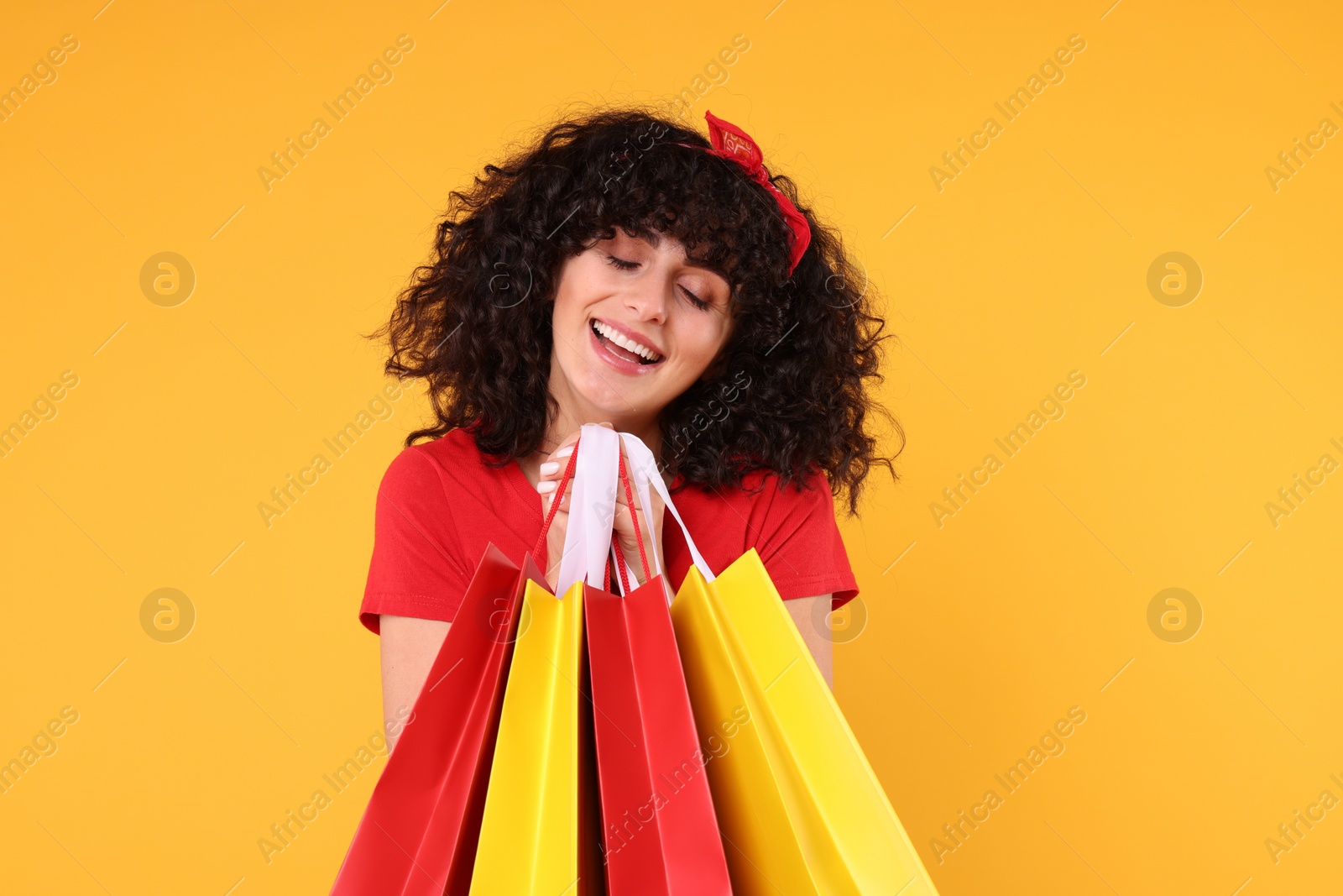 Photo of Happy young woman with shopping bags on yellow background