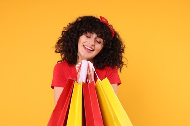 Happy young woman with shopping bags on yellow background