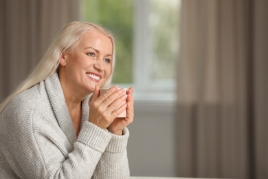 Portrait of beautiful older woman with cup of tea against blurred background. Space for text