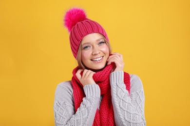 Photo of Young woman in warm sweater, scarf and hat on yellow background. Winter season