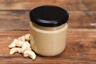 Tasty nut paste in jar and cashews on wooden table, closeup