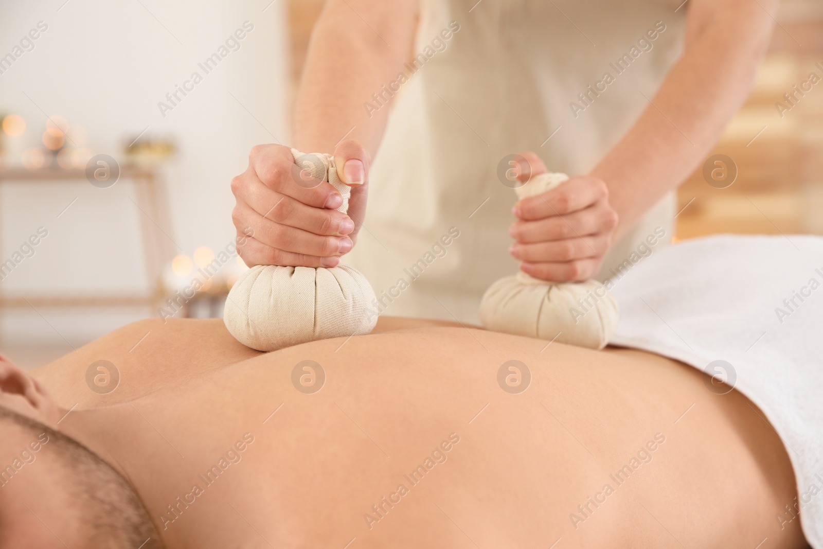 Photo of Handsome man receiving herbal bag massage in spa salon, closeup