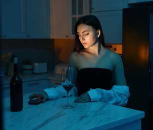 Beautiful woman with smartphone and wine in kitchen at night