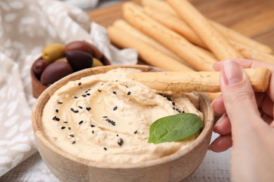 Photo of Woman dipping tasty grissini stick into hummus at white wooden table, closeup