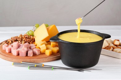 Photo of Dipping piece of ham into fondue pot with tasty melted cheese at white wooden table