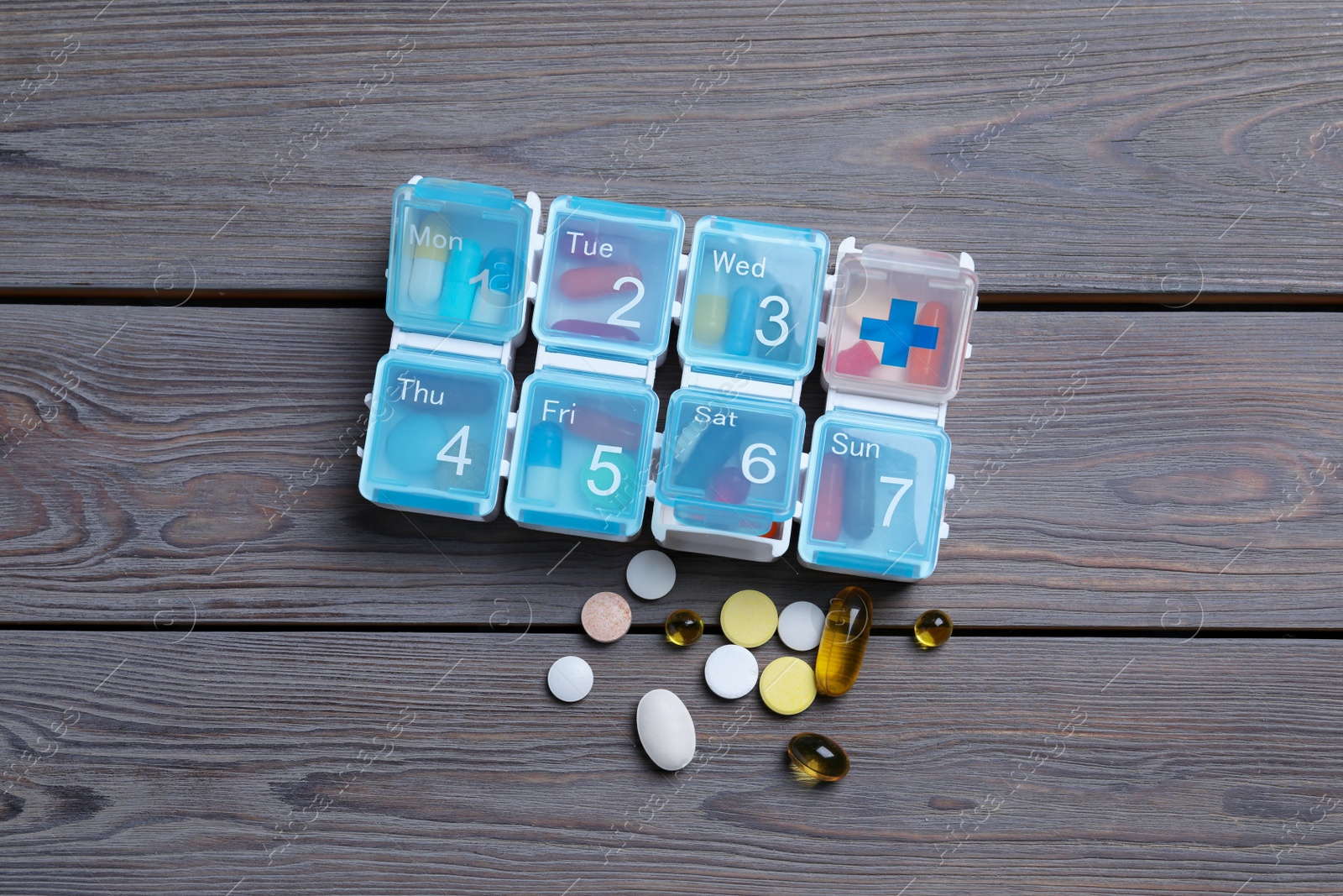 Photo of Weekly pill box with medicaments on wooden table, flat lay