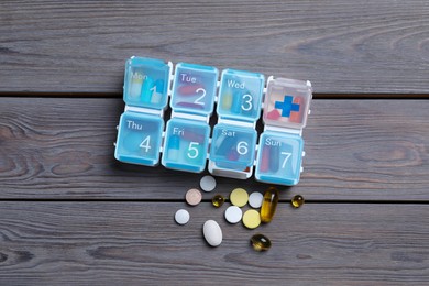 Weekly pill box with medicaments on wooden table, flat lay