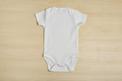 Cute baby onesie on wooden background, top view