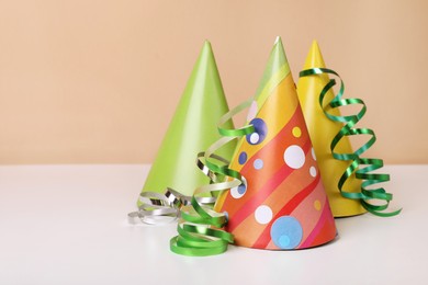 Colorful party hats and streamers on white table, space for text. Birthday celebration