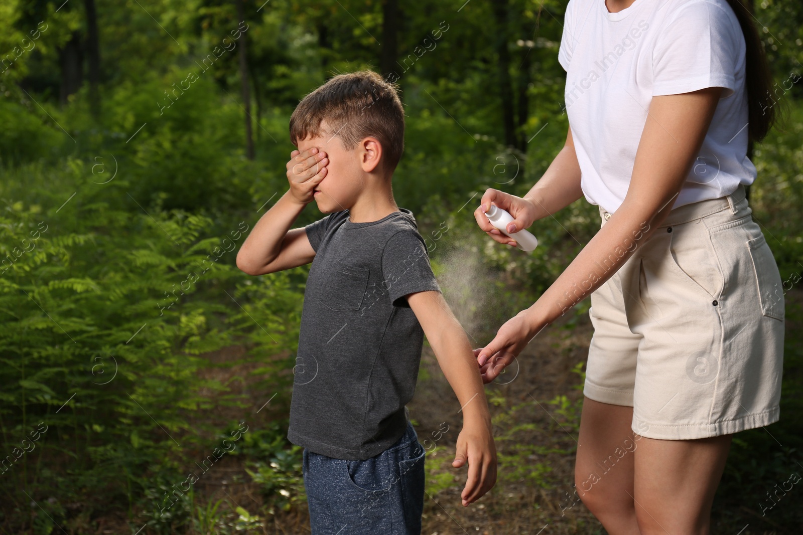 Photo of Woman applying insect repellent on her son's arm in park. Tick bites prevention