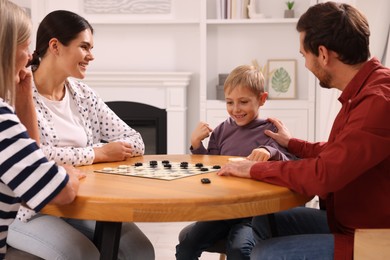 Photo of Family playing checkers at coffee table in room. Boy enjoying winning