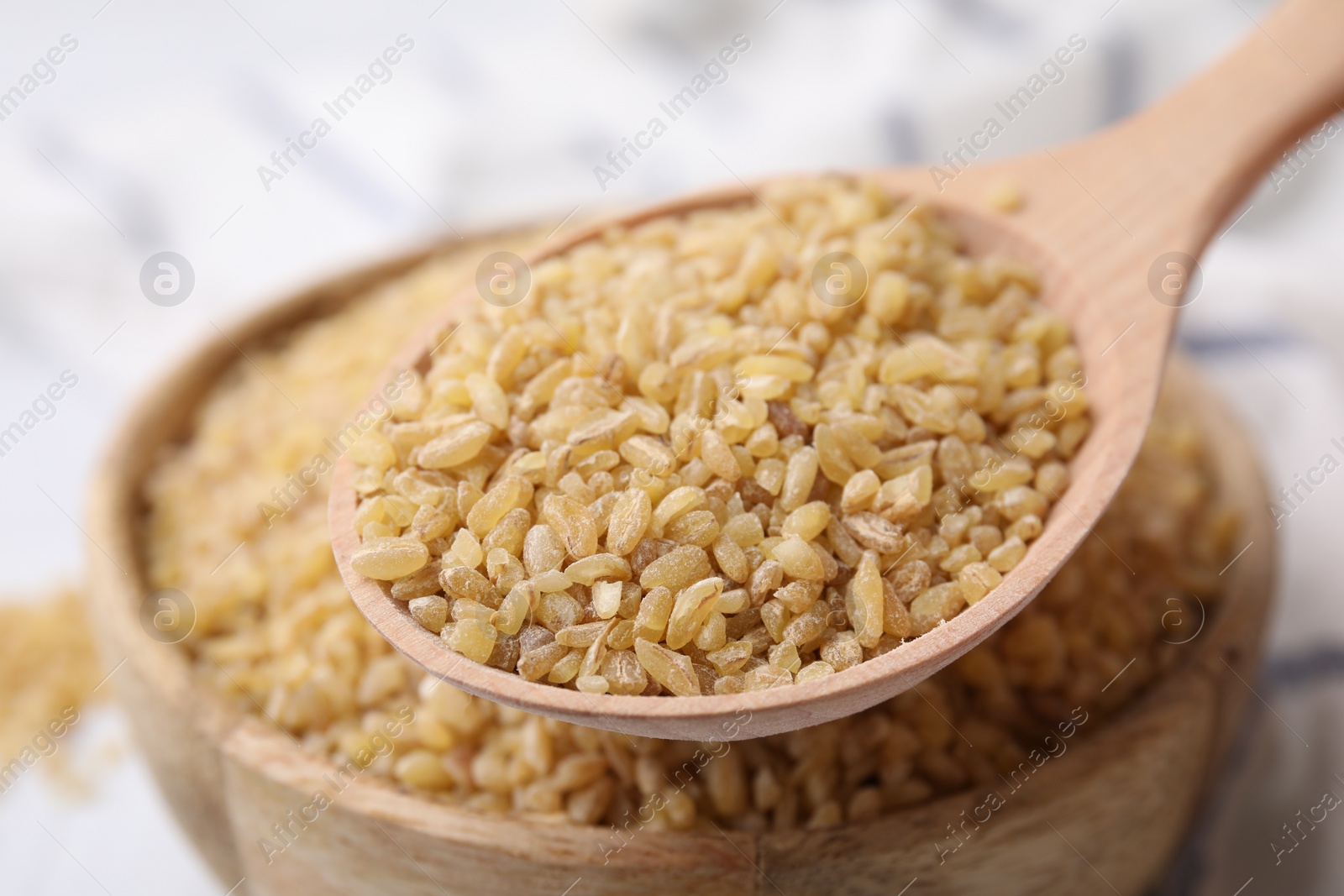 Photo of Taking raw bulgur with spoon from bowl on table, closeup