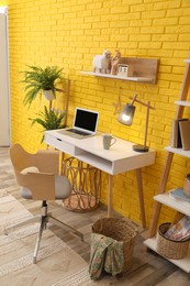 Modern workplace interior with wooden furniture and laptop near yellow brick wall