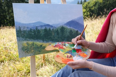 Photo of Young woman drawing on easel with brush outdoors, closeup