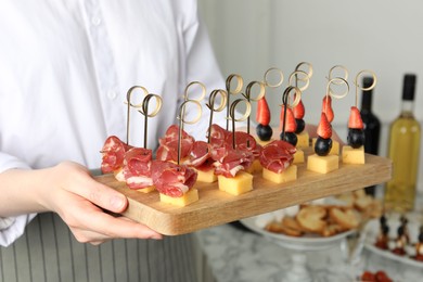 Photo of Woman holding tray of different tasty canapes indoors, closeup