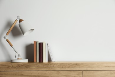 Photo of Stylish lamp and books on wooden table near white wall, space for text. Interior design