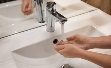 Woman washing hands under tap indoors, closeup