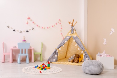 Photo of Cozy child room interior with play tent, table and modern decor elements