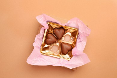 Partially empty box of chocolate candies on light brown background, top view
