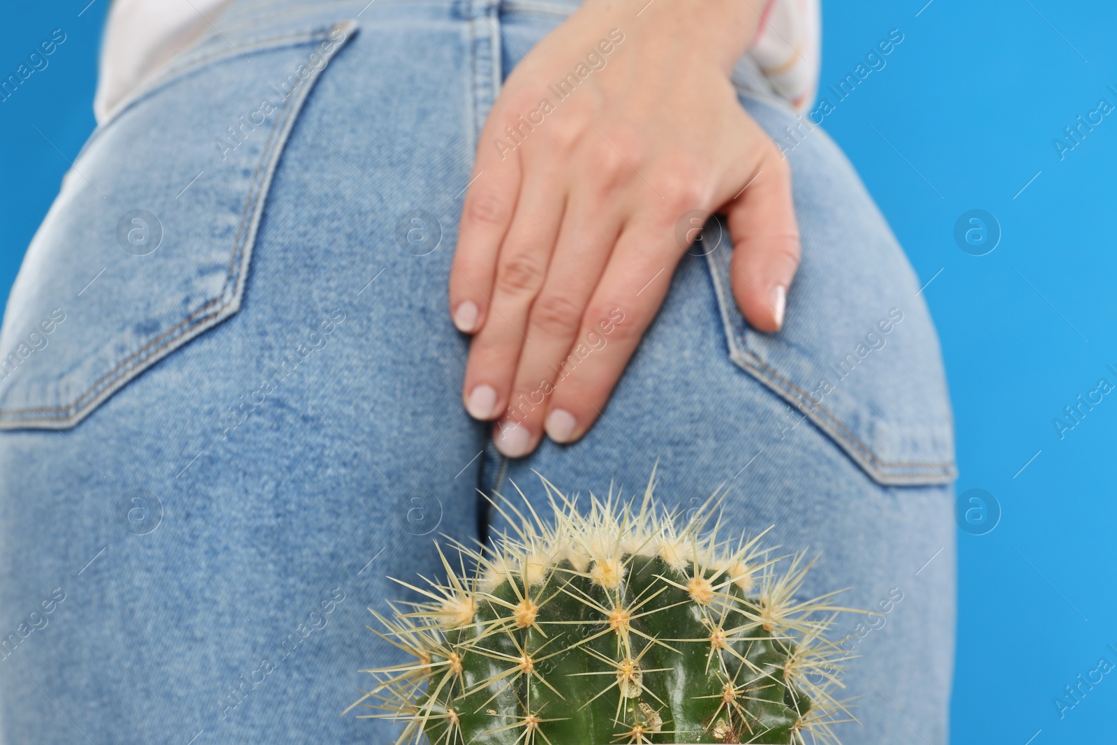 Photo of Woman sitting down on cactus against light blue background, closeup. Hemorrhoid concept