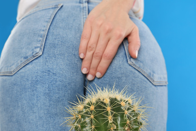 Photo of Woman sitting down on cactus against light blue background, closeup. Hemorrhoid concept