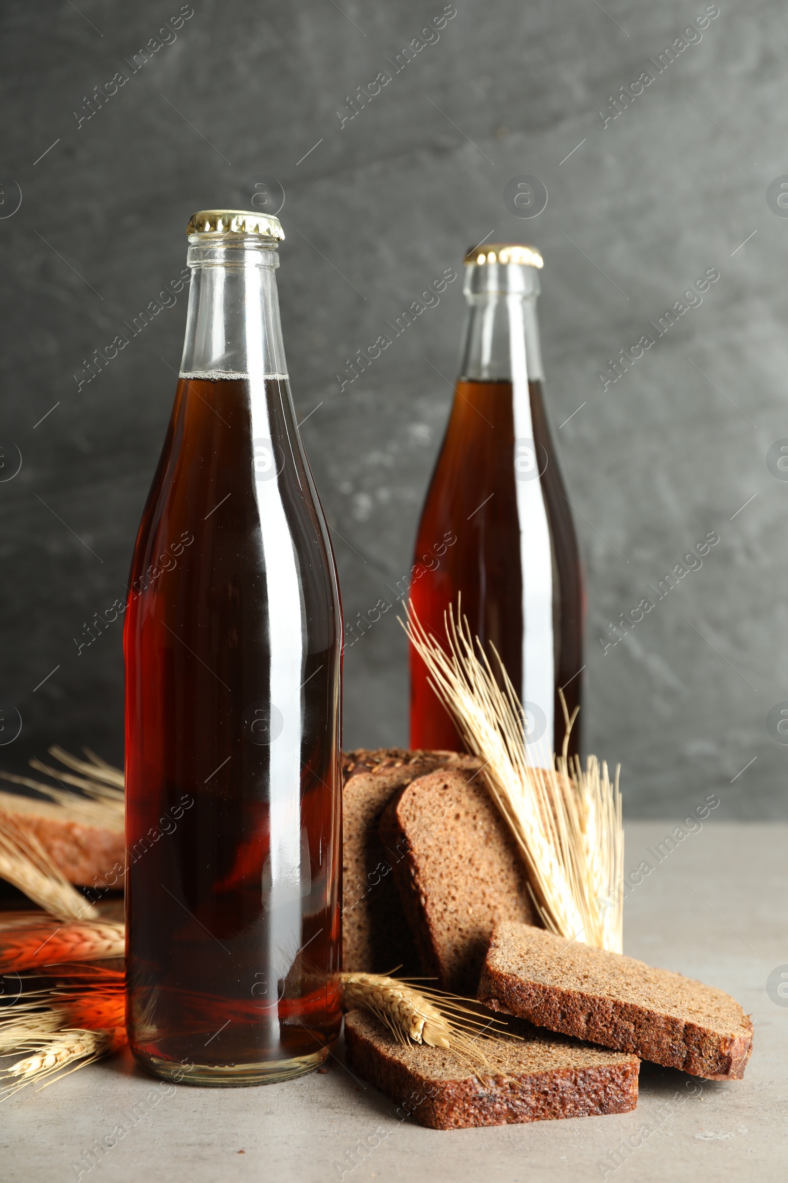 Photo of Bottle of delicious fresh kvass, spikelets and bread on grey table