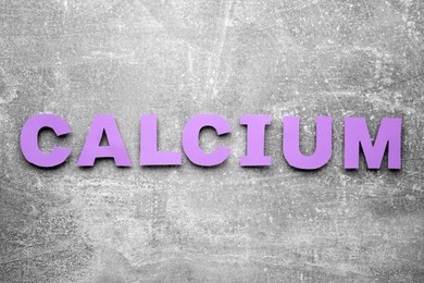 Photo of Word Calcium made of violet paper letters on gray background, top view
