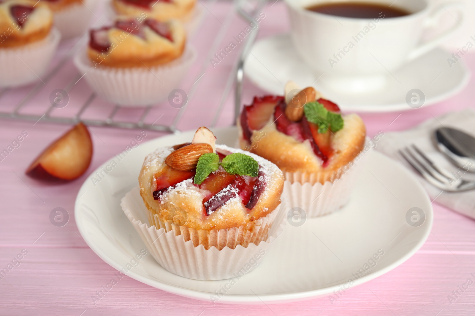 Photo of Delicious cupcakes with plums on pink wooden table, closeup