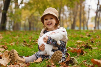 Photo of Girl sitting with cute white rabbit on grass in autumn park