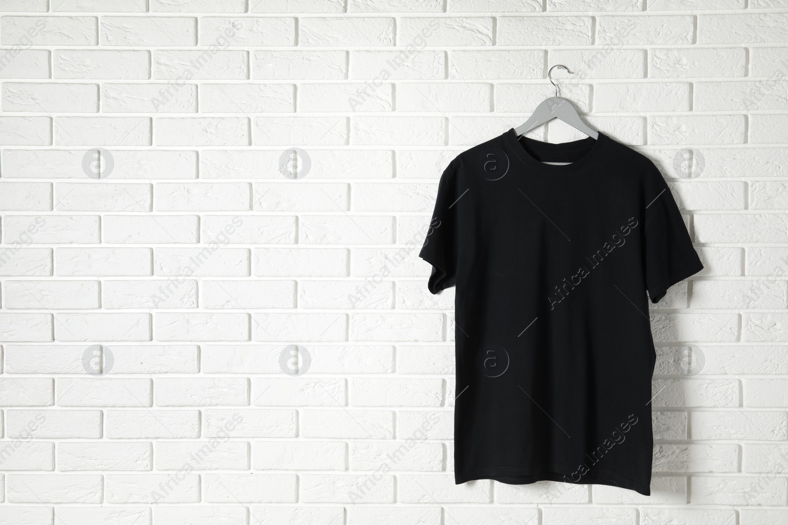 Photo of Hanger with black t-shirt against brick wall. Mockup for design