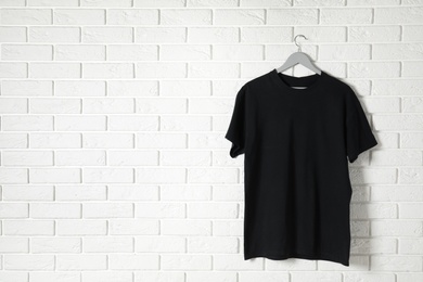 Photo of Hanger with black t-shirt against brick wall. Mockup for design