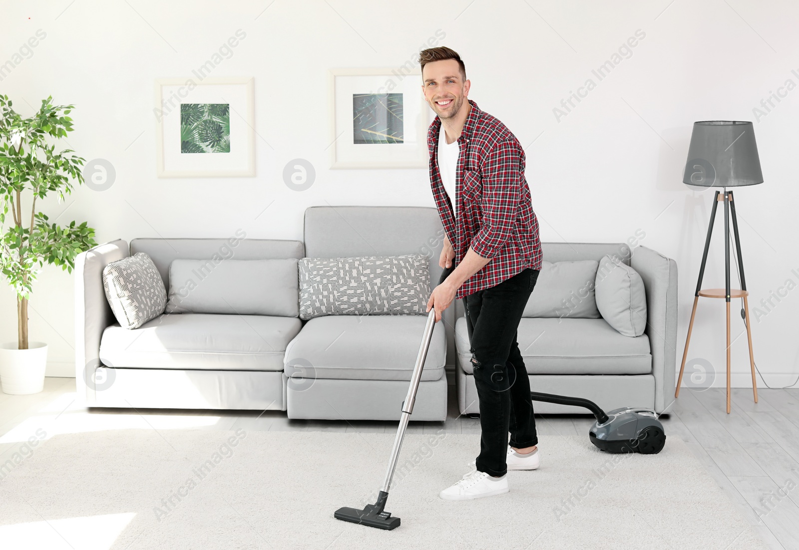 Photo of Young man removing dirt from carpet with vacuum cleaner at home