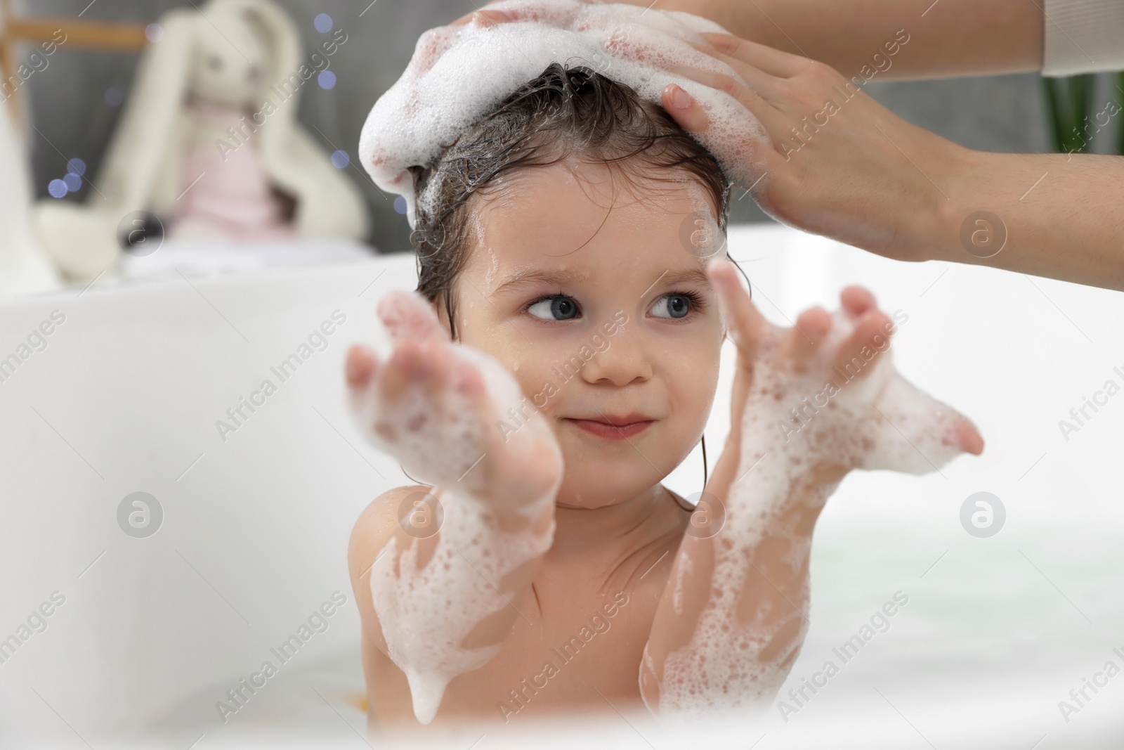 Photo of Cute little girl washing hair with shampoo in bathroom