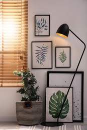 Photo of Stylish room interior with green eucalyptus tree, floral paintings and lamp