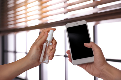 Image of Woman sanitizing smartphone with antiseptic spray indoors, closeup. Be safety during coronavirus outbreak 