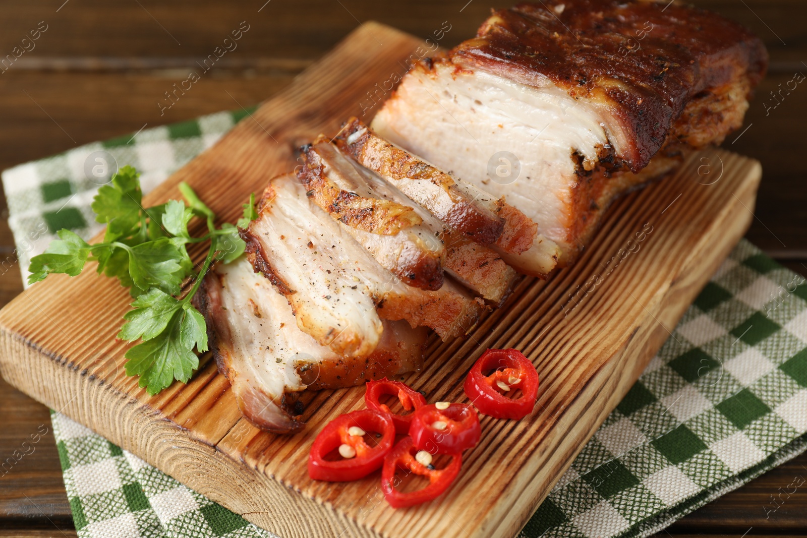 Photo of Pieces of baked pork belly served with chili pepper and parsley on wooden table, closeup