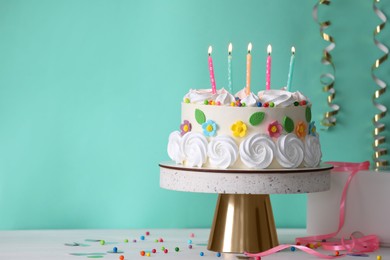 Photo of Delicious birthday cake and party decor on white wooden table against turquoise background, space for text