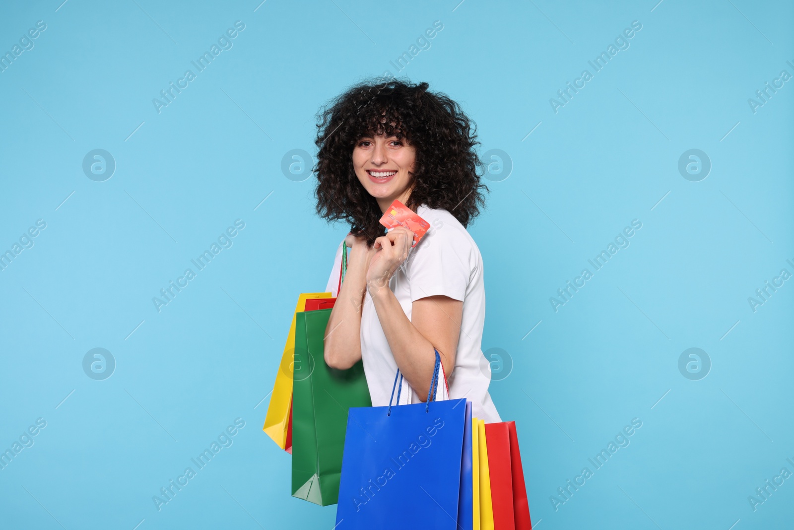 Photo of Happy young woman with shopping bags and credit cards on light blue background