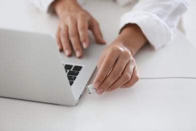 Photo of Woman connecting charger cable to laptop at white table, closeup