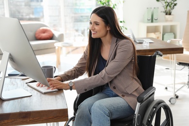 Young woman in wheelchair using computer at workplace