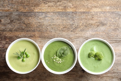 Dishes with different fresh vegetable detox soups made of green peas, broccoli and spinach on wooden background, flat lay. Space for text